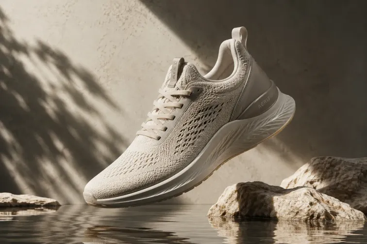 Scarpa sportiva bianca sospesa sopra acqua e rocce in un'ambientazione dai toni naturali